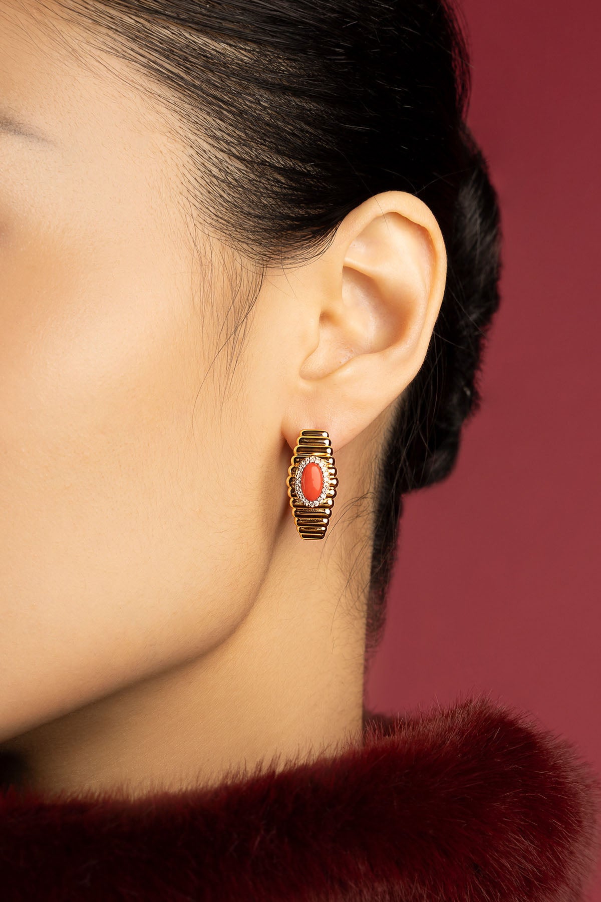 Woman wearing APM Monaco earrings, a golden glow with coral warmth.
