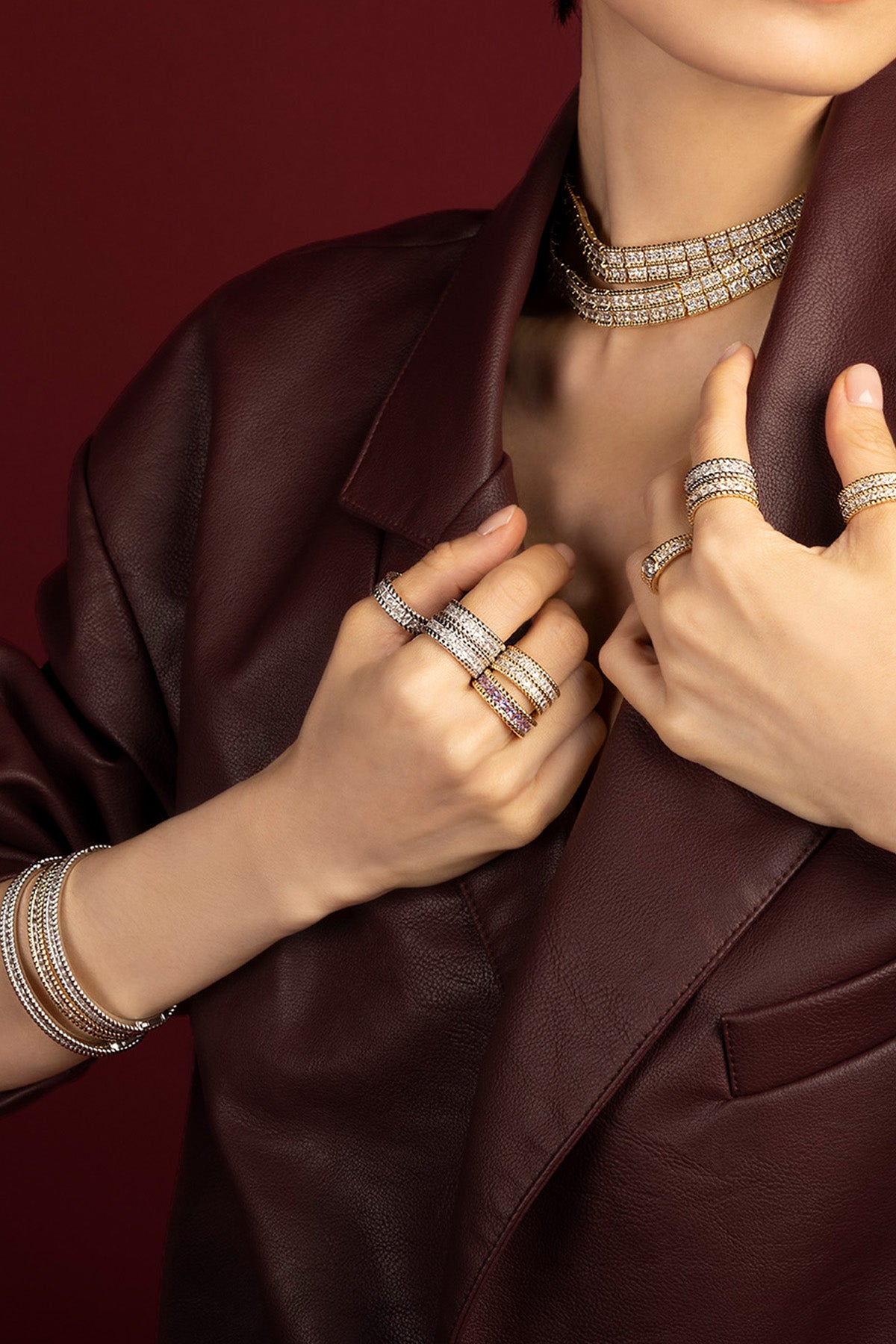 Woman wearing APM Monaco stacked jewelry, a bold shimmer against burgundy leather.