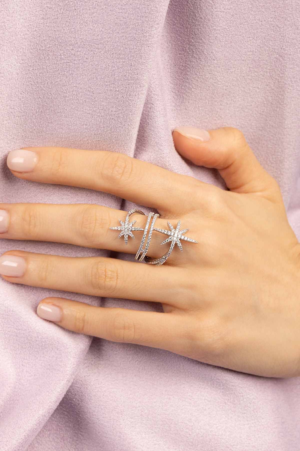 Hand wearing APM MONACO Silver-tone ring with star design on a light purple fabric background