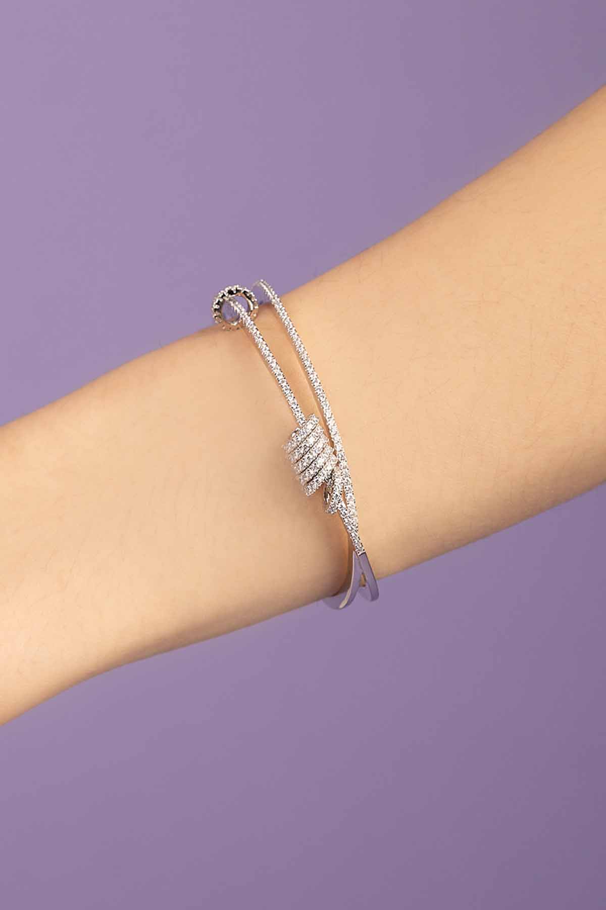 APM MONACO Silver-tone cuff with sliding rings on a person's wrist against a purple background