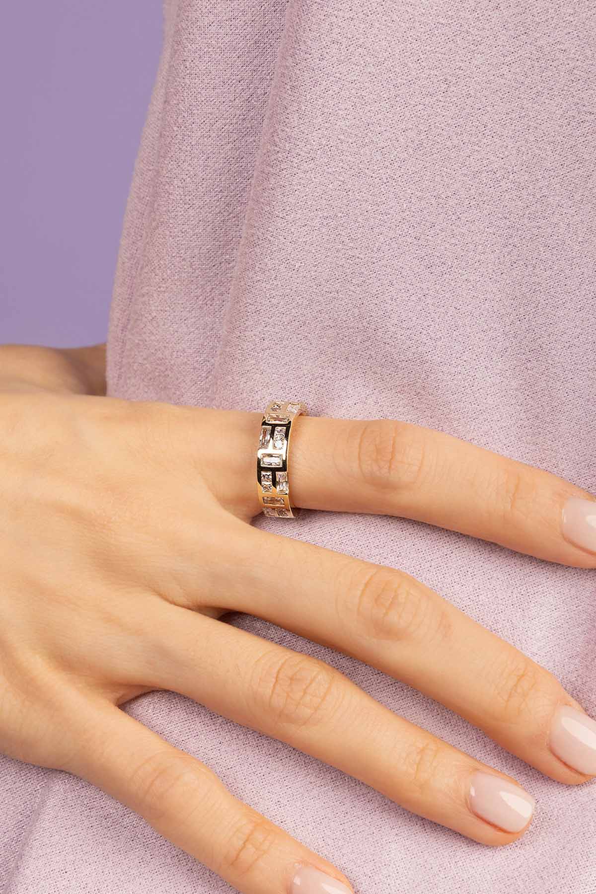 Hand wearing APM MONACO ice ring in yellow gold on a light purple background