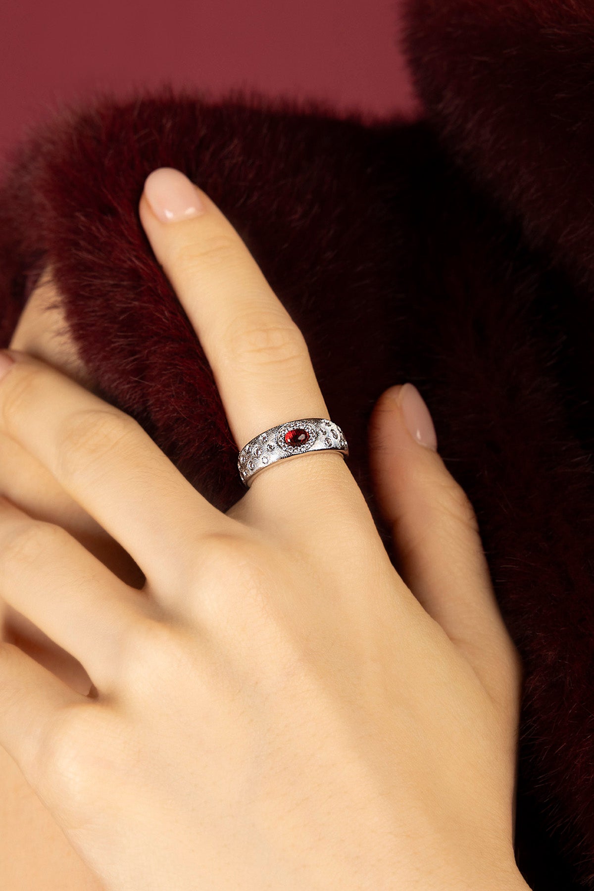 Woman wearing APM Monaco ring, a red spark against velvet warmth.