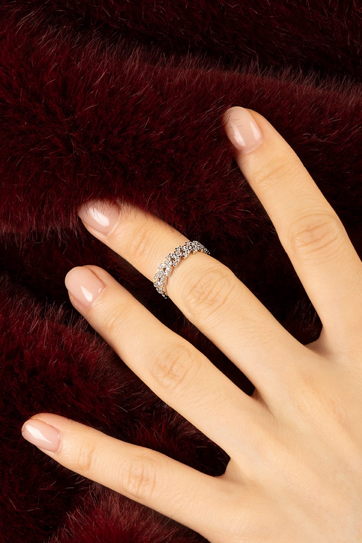 Woman wearing APM Monaco ring, a delicate sparkle against plush burgundy.
