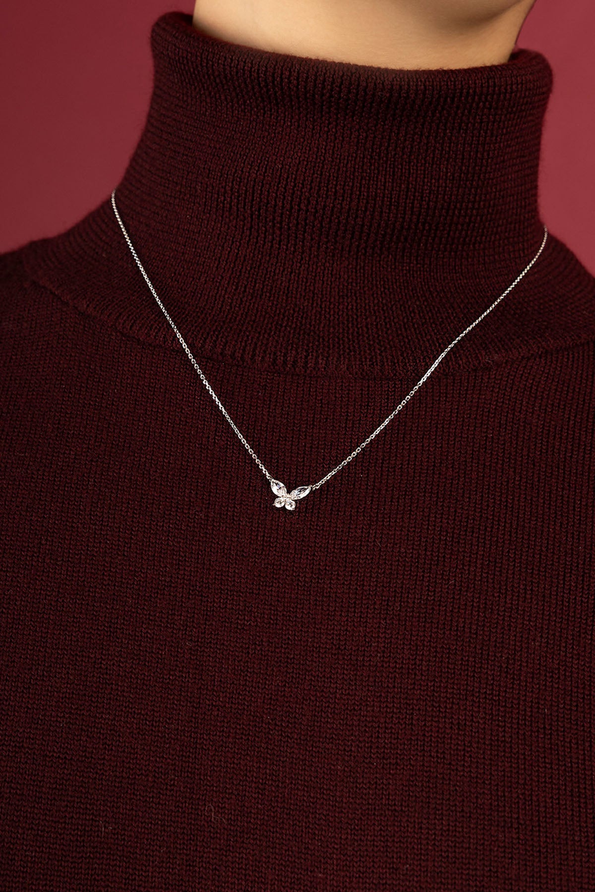 Woman wearing APM butterfly necklace, a delicate flutter over burgundy knitwear.