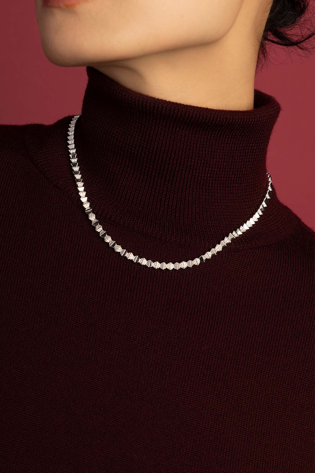 Woman wearing APM necklace, a sharp geometric glow against warm burgundy.