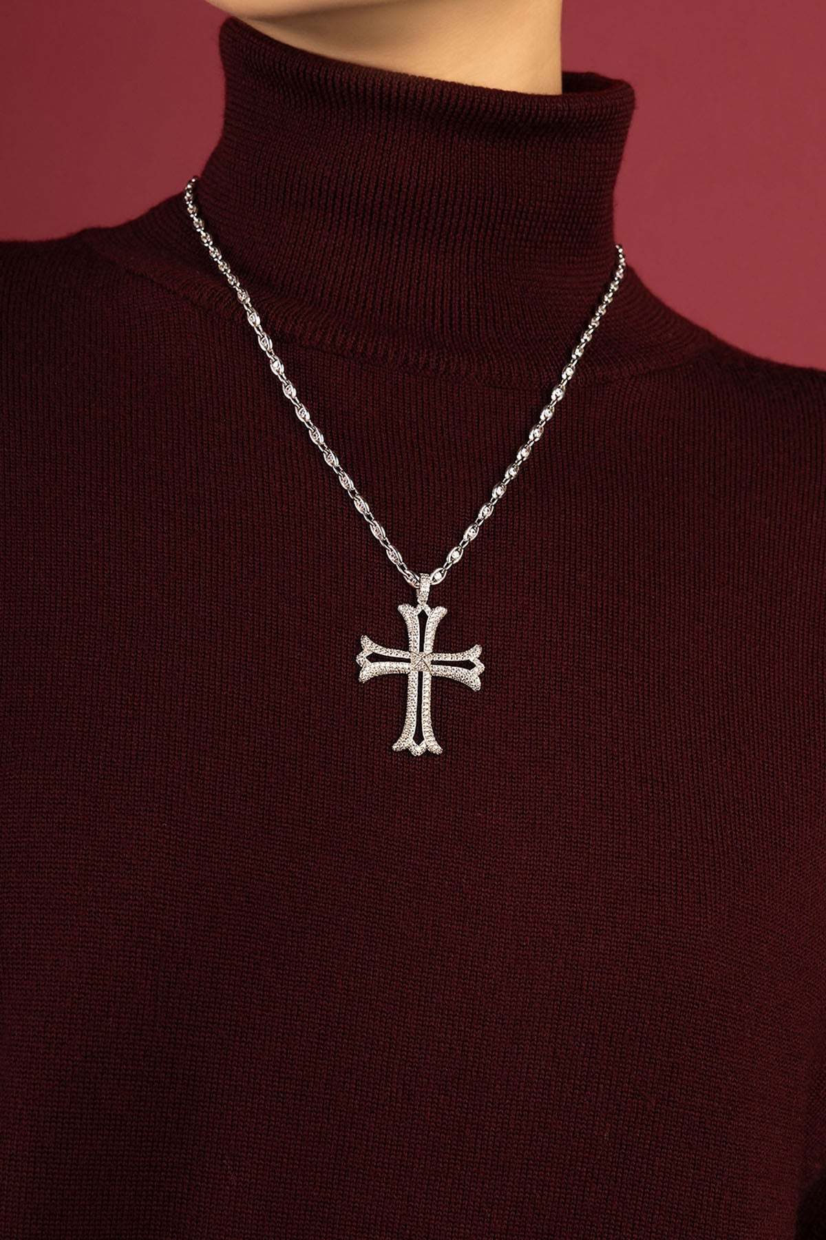 Woman wearing APM cross necklace, a bold statement over burgundy knitwear.