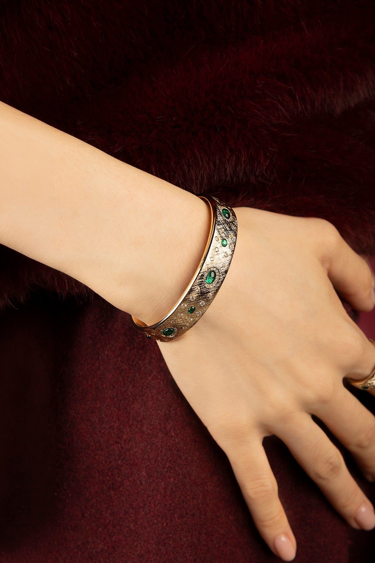 Woman wearing APM Monaco bangle, emerald whispers on a vintage-inspired glow.