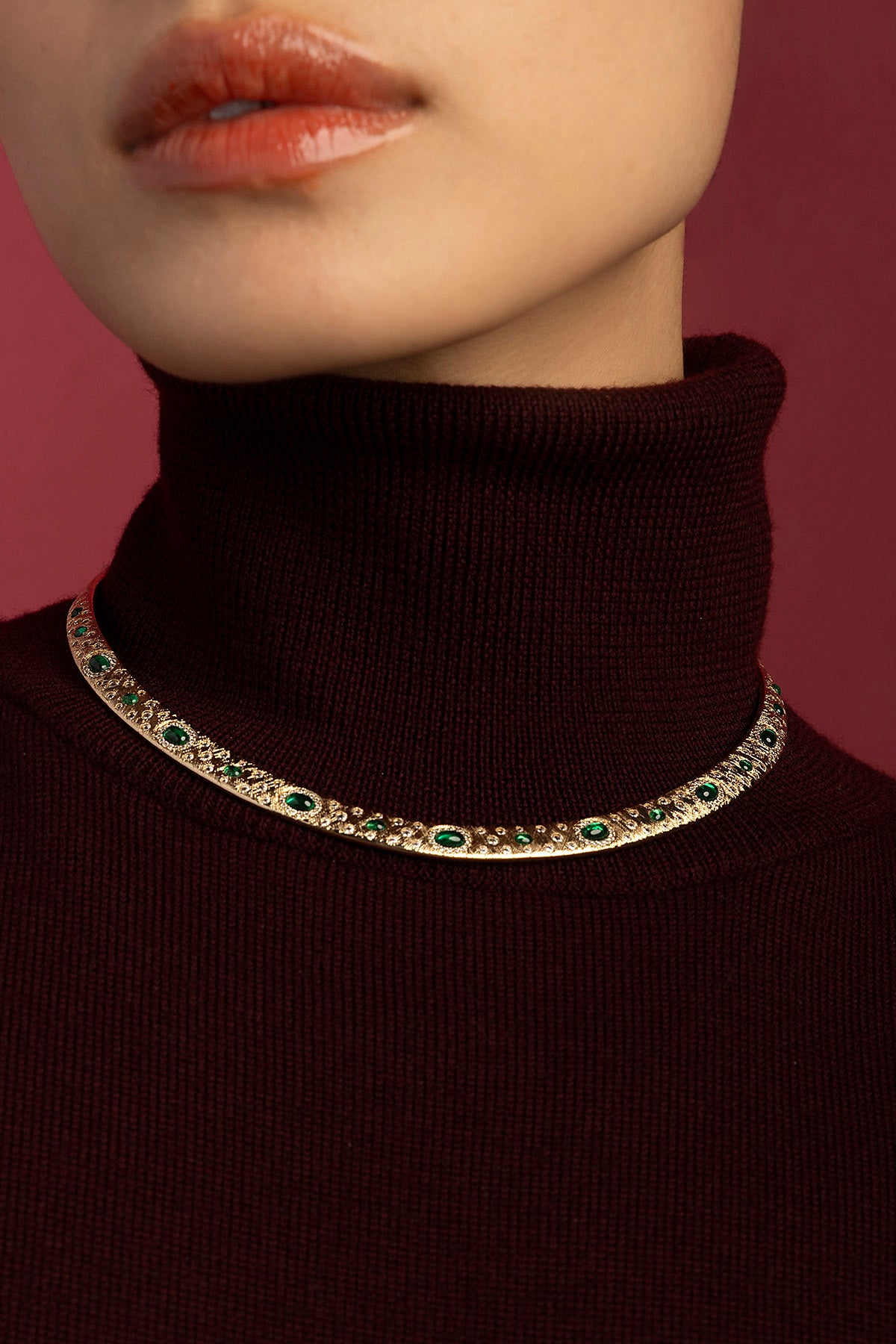 Woman wearing APM Monaco necklace, emerald hues glowing against burgundy warmth.