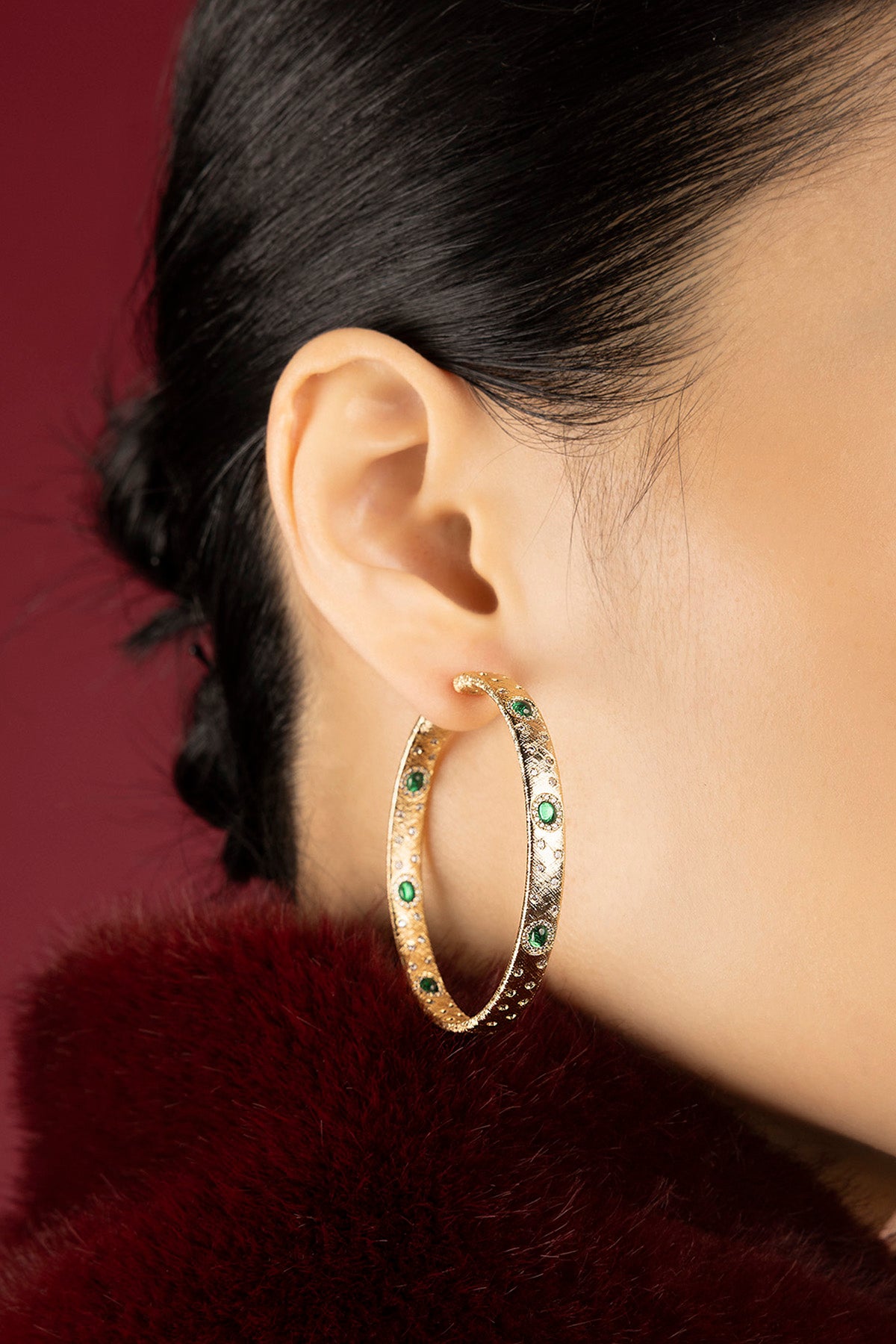 Woman wearing APM Monaco hoop earrings, golden allure touched with emerald green sparks.