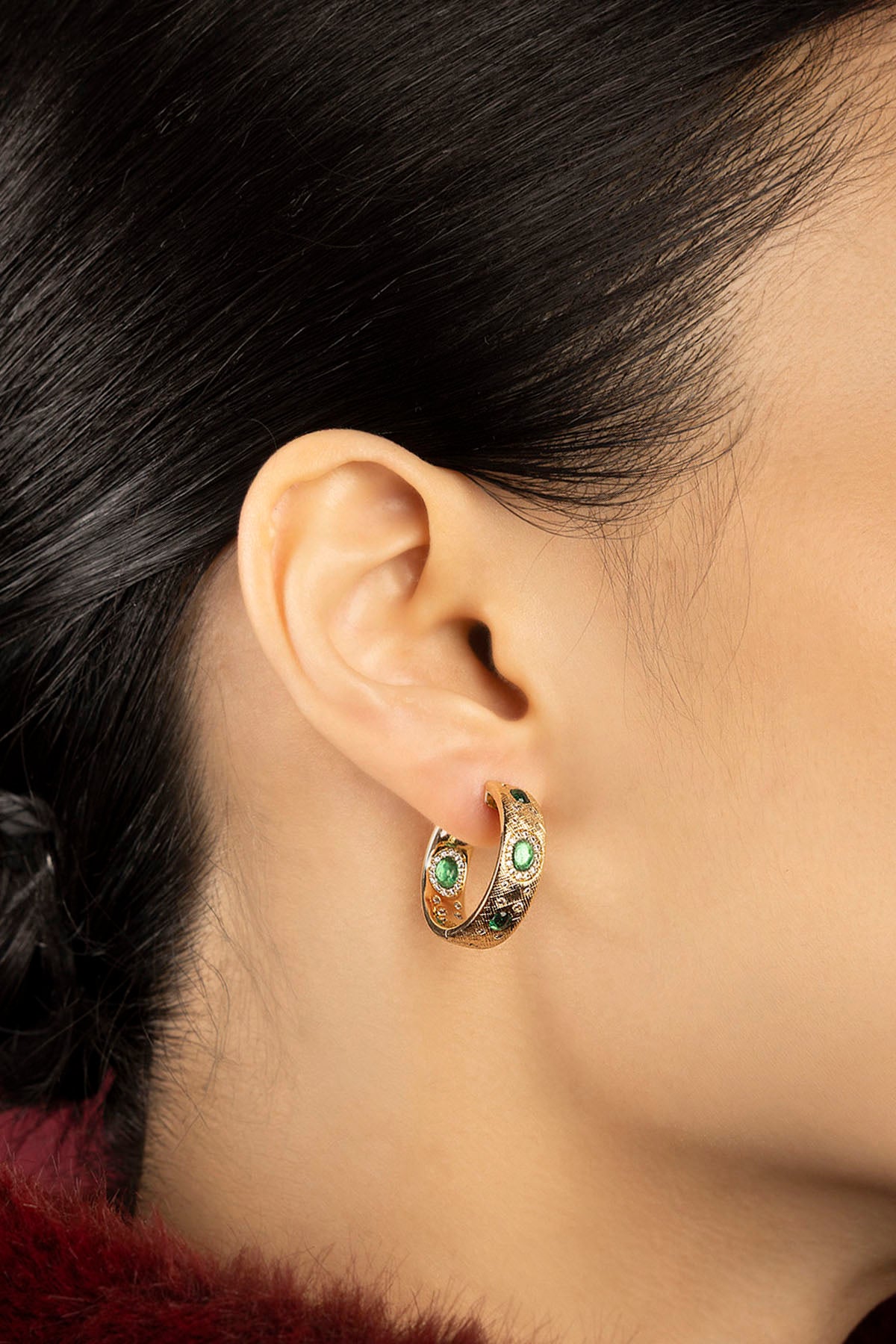 Woman wearing APM Monaco hoop earrings, green accents glowing with quiet elegance.