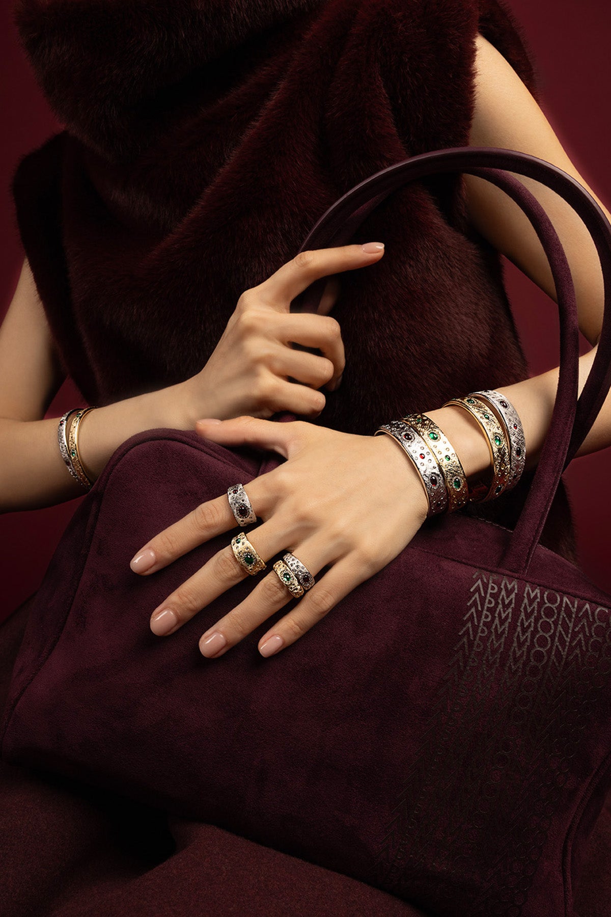 Woman wearing APM Bangles and Rings, a rich stack glowing against burgundy.