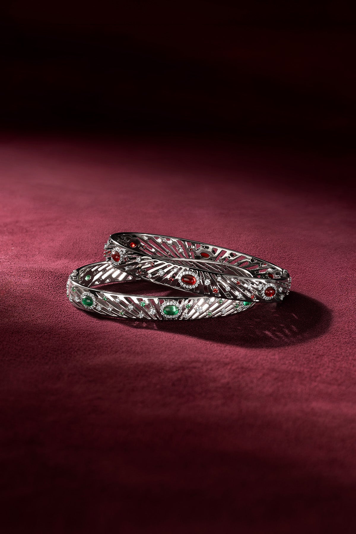 APM Bangles in rhodium finish, sculpted feathers glowing with emerald and ruby whispers.