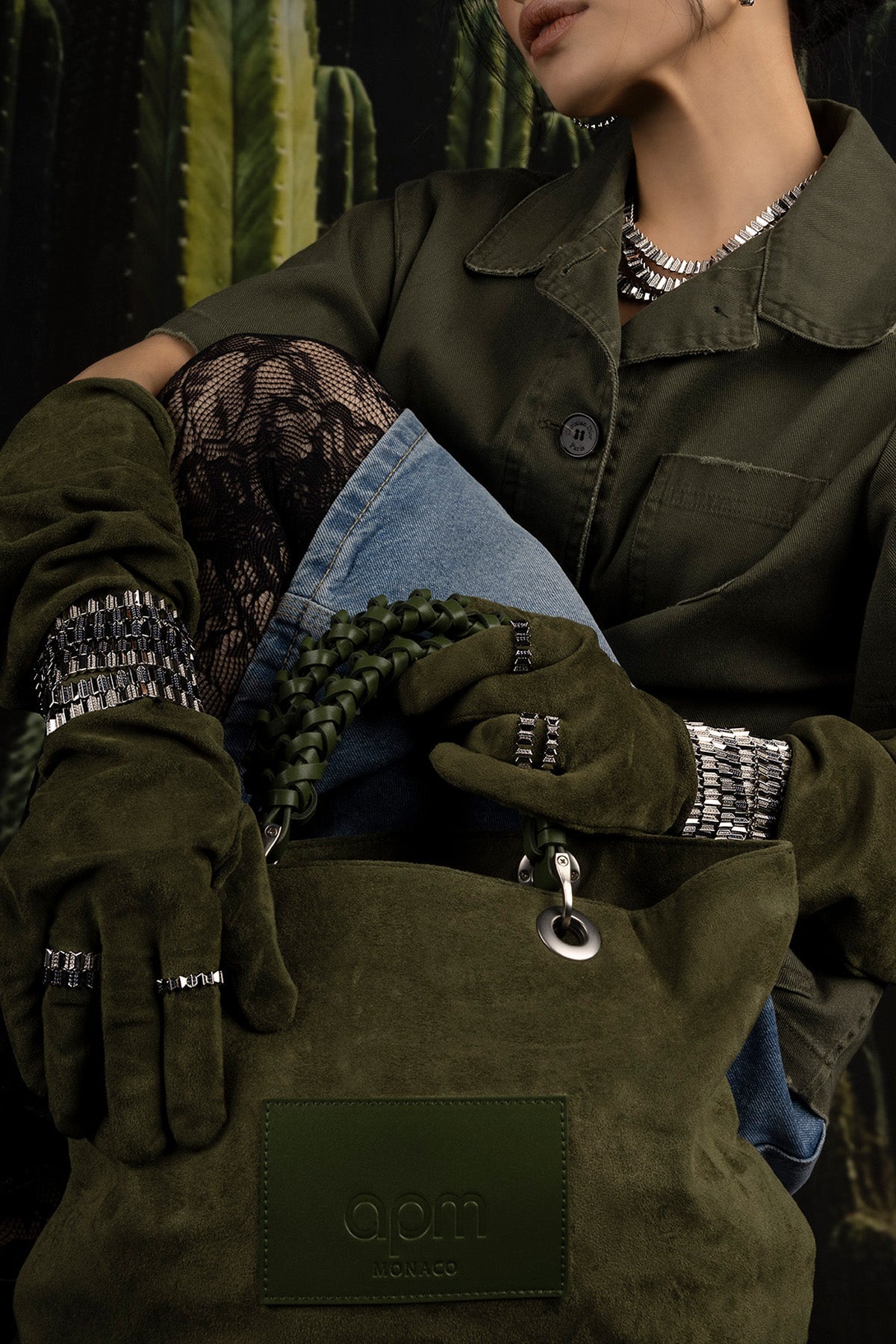 Model is wearing APM Monaco Up and down ring in Dark Grey on green gloves and coat with a cactus plant in the background