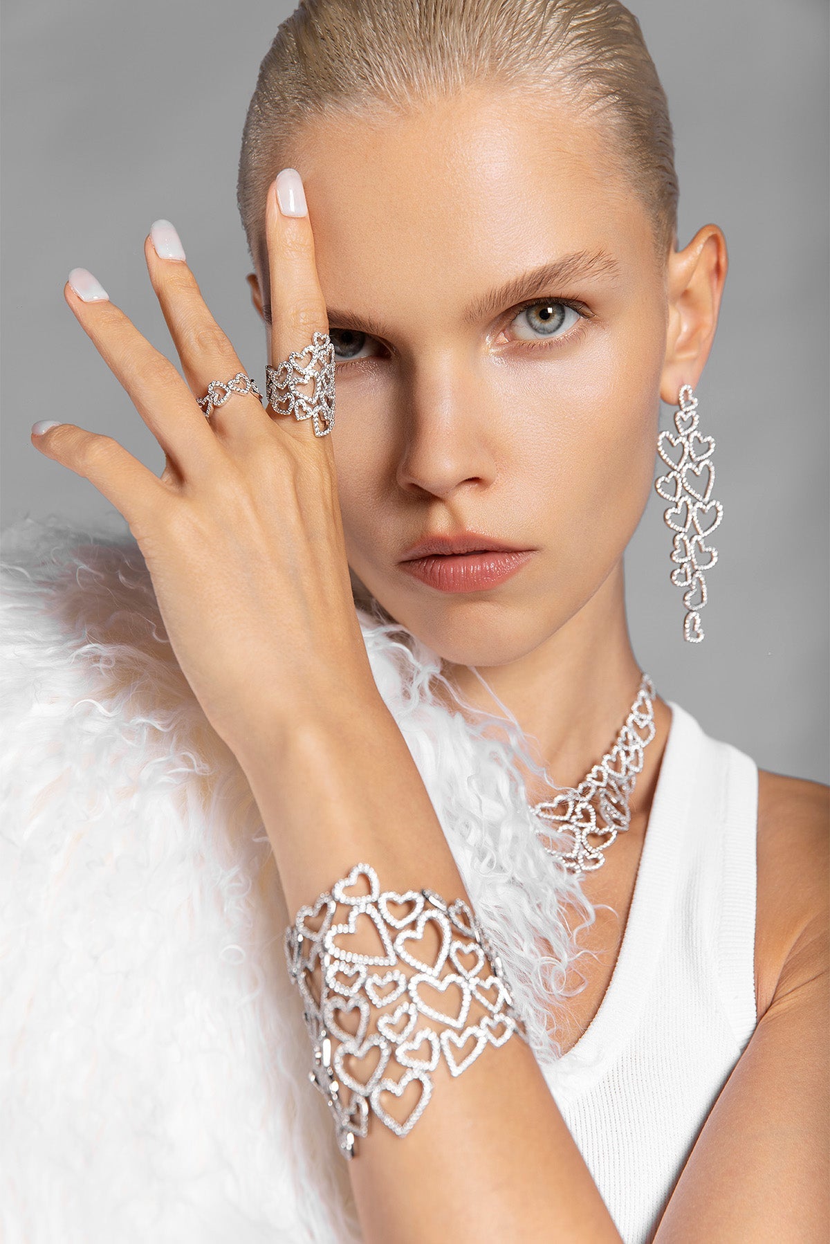 Woman wearing APM MONACO silver heart-shaped jewelry including a ring, bracelet, and earrings on a gray background