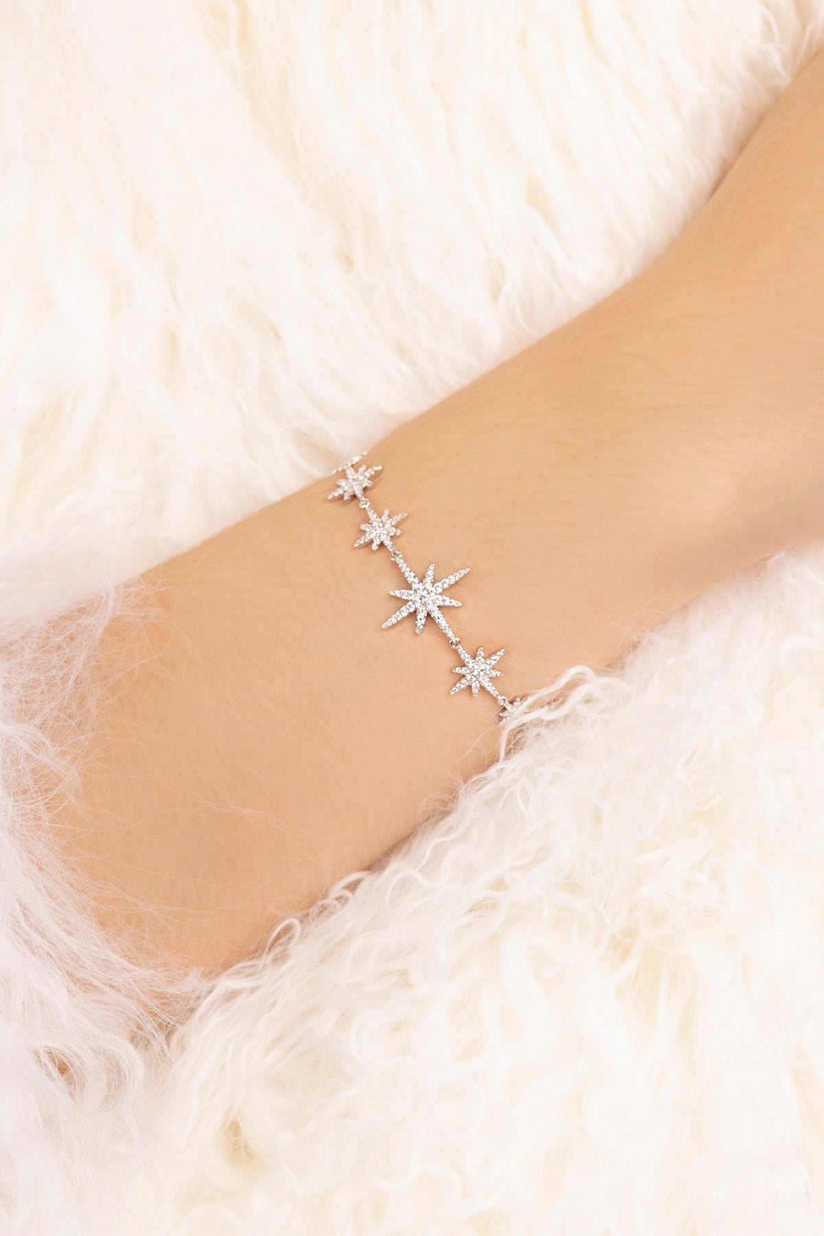 Silver star bracelet on a person's wrist against a white fur background