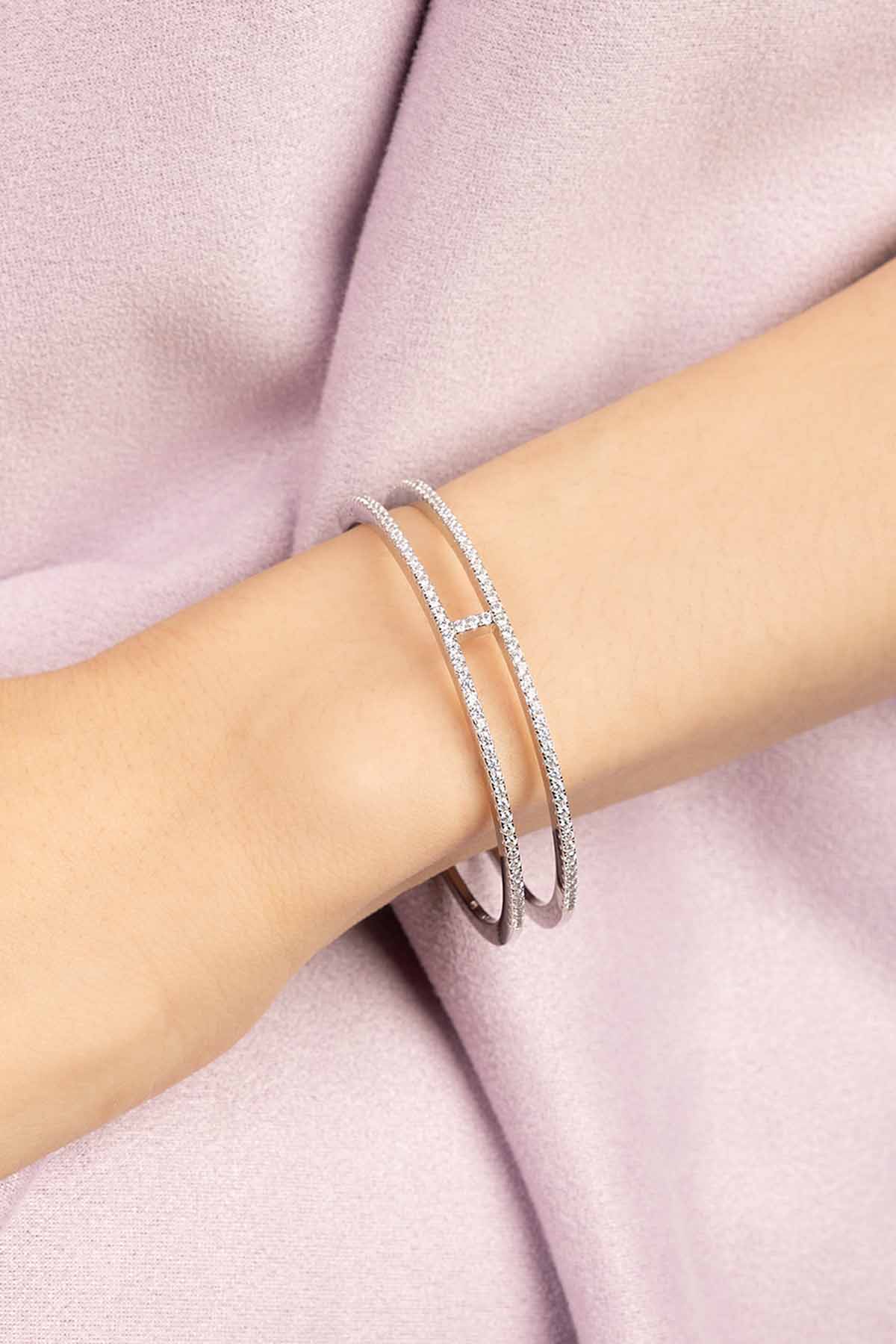 APM MONACO silver cuff with double line design on a person's wrist against a purple fabric background