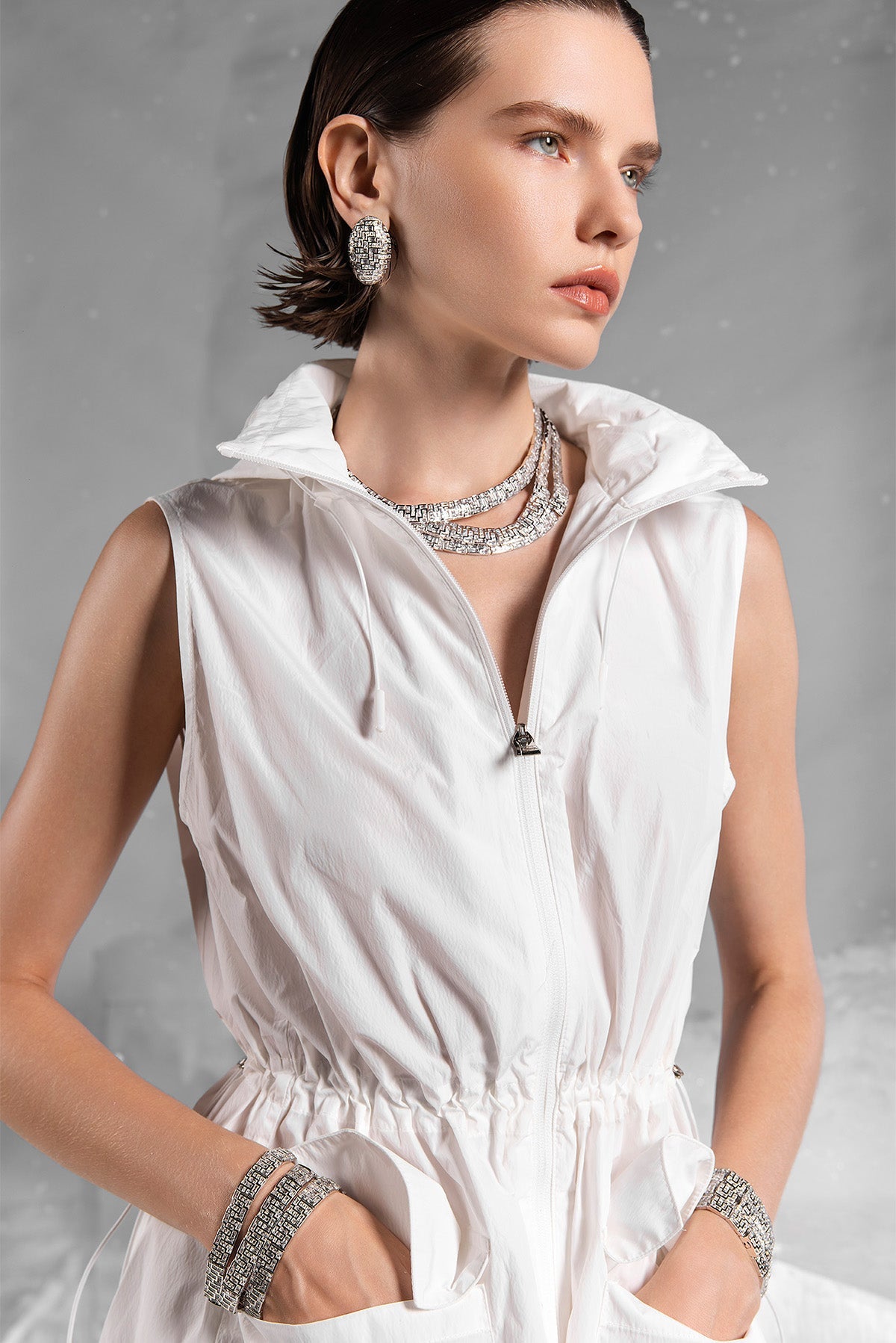 Woman wearing a white sleeveless top with APM MONACO labyrinth jewelry on a gray background
