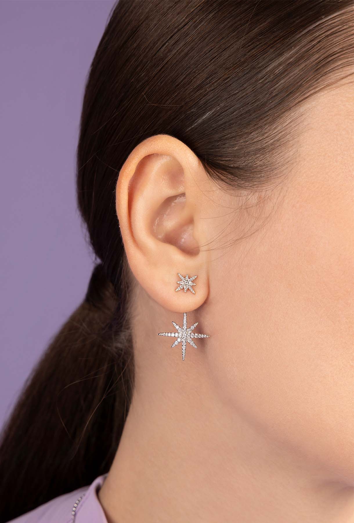 Close-up of a person wearing silver star-shaped earrings against a purple background