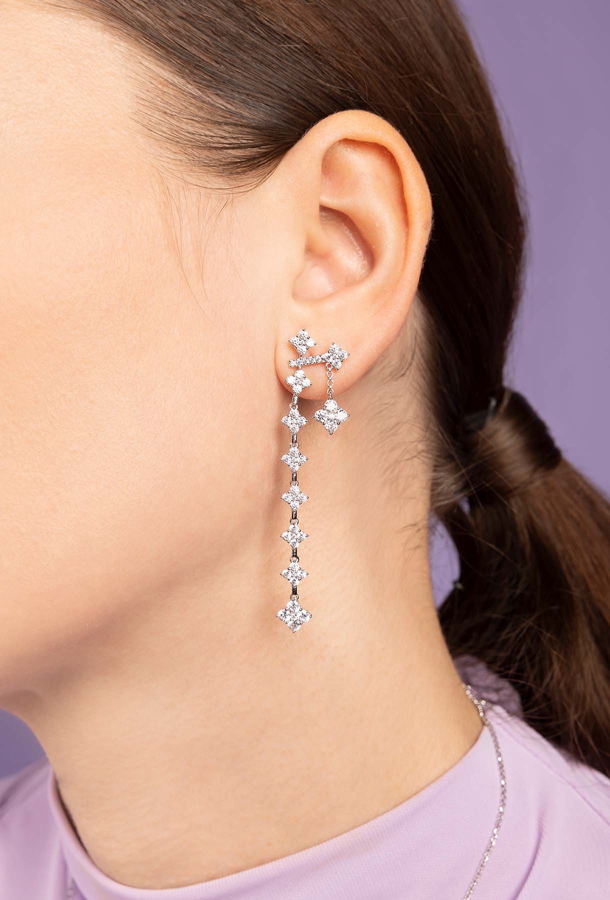 Close-up of a person wearing a delicate silver earring with clear stones against a neutral background