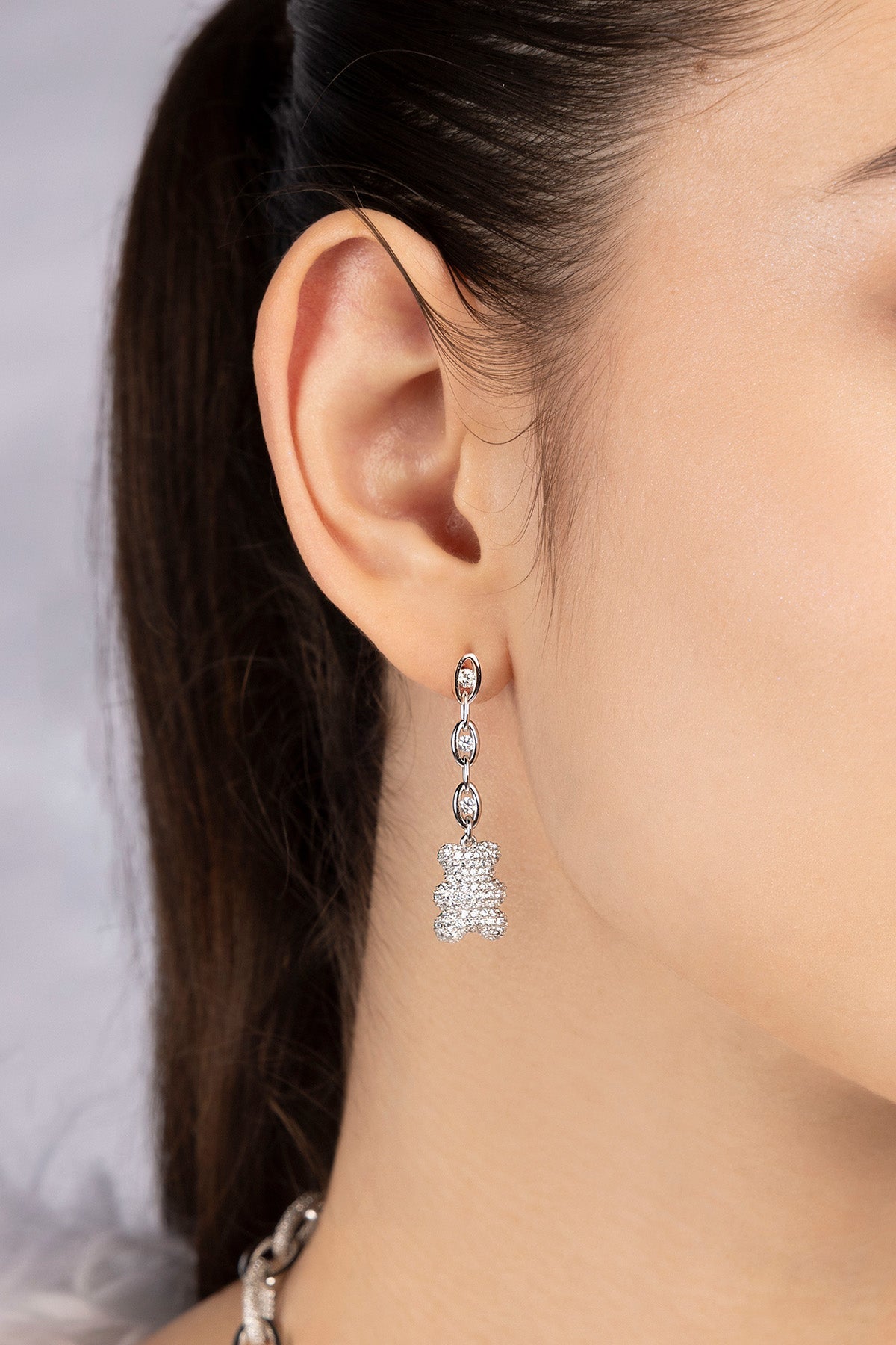 Close-up of a person wearing mint yummy bear drop earrings from APM MONACO with a neutral background