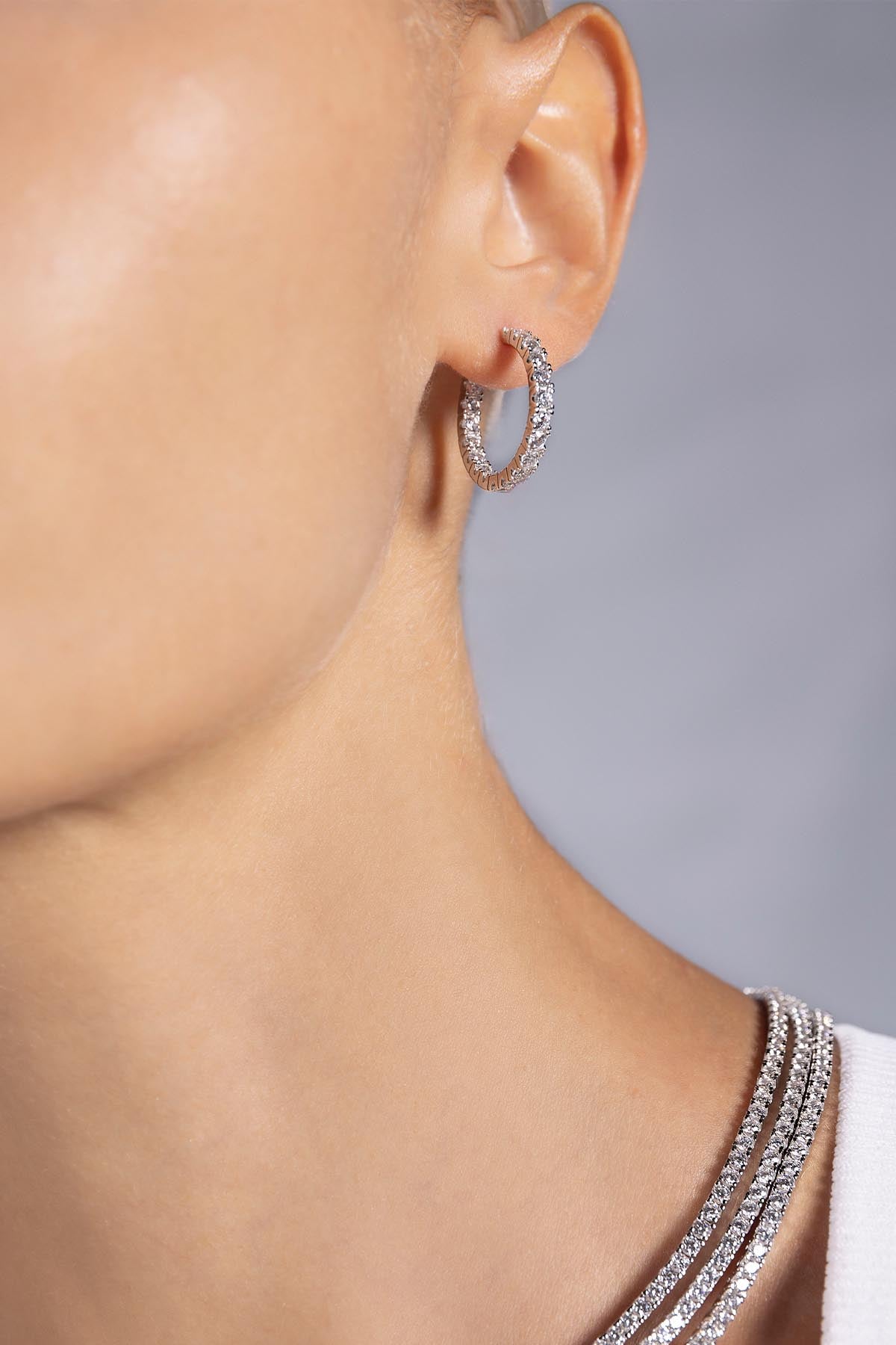 Close-up of a person wearing silver hoop earrings from APM MONACO with a neutral background
