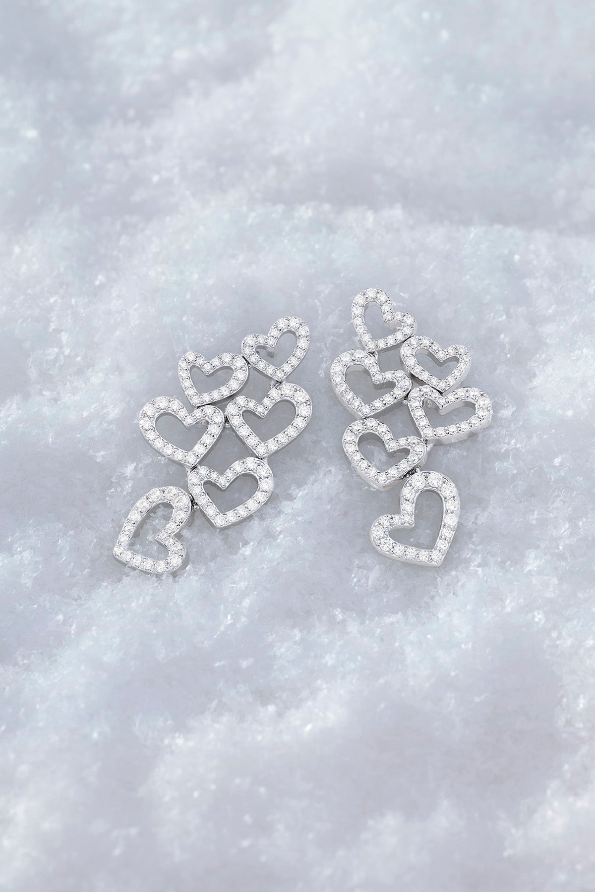 APM MONACO heart-shaped earrings in silver on a textured white surface
