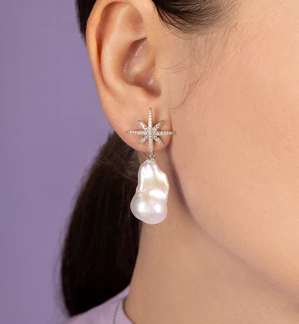 Close-up of an ear wearing a APM MONACO star-shaped earring with a pearl drop against a purple background