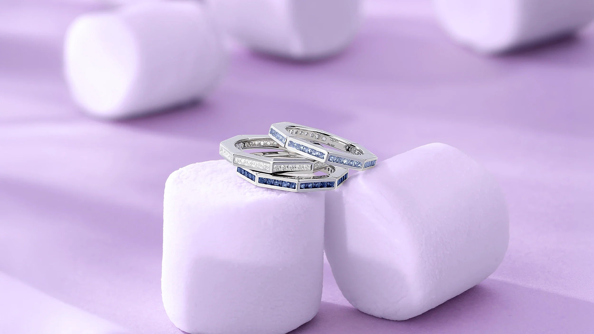 Three APM MONACO Geometric line rings with blue and white stones on purple marshmallows