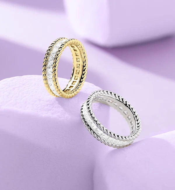 Two APM MONACO yellow gold and silver torsade rings on a light purple background