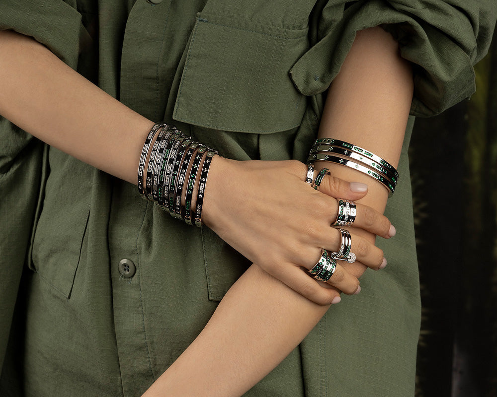 Close-up of a person wearing multiple apm monaco morse code bracelets and rings on an olive green shirt background