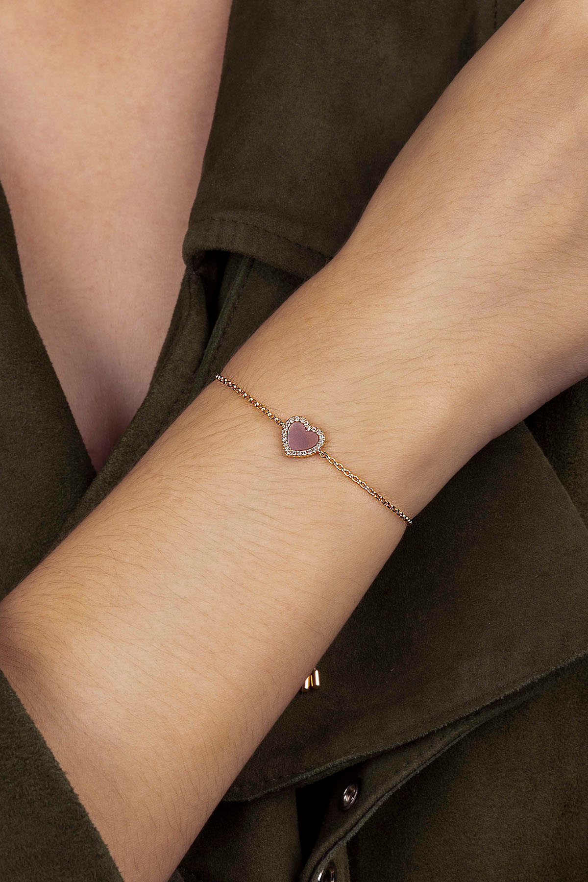 Close-up of a wrist wearing a delicate bracelet with a heart-shaped pink stone.