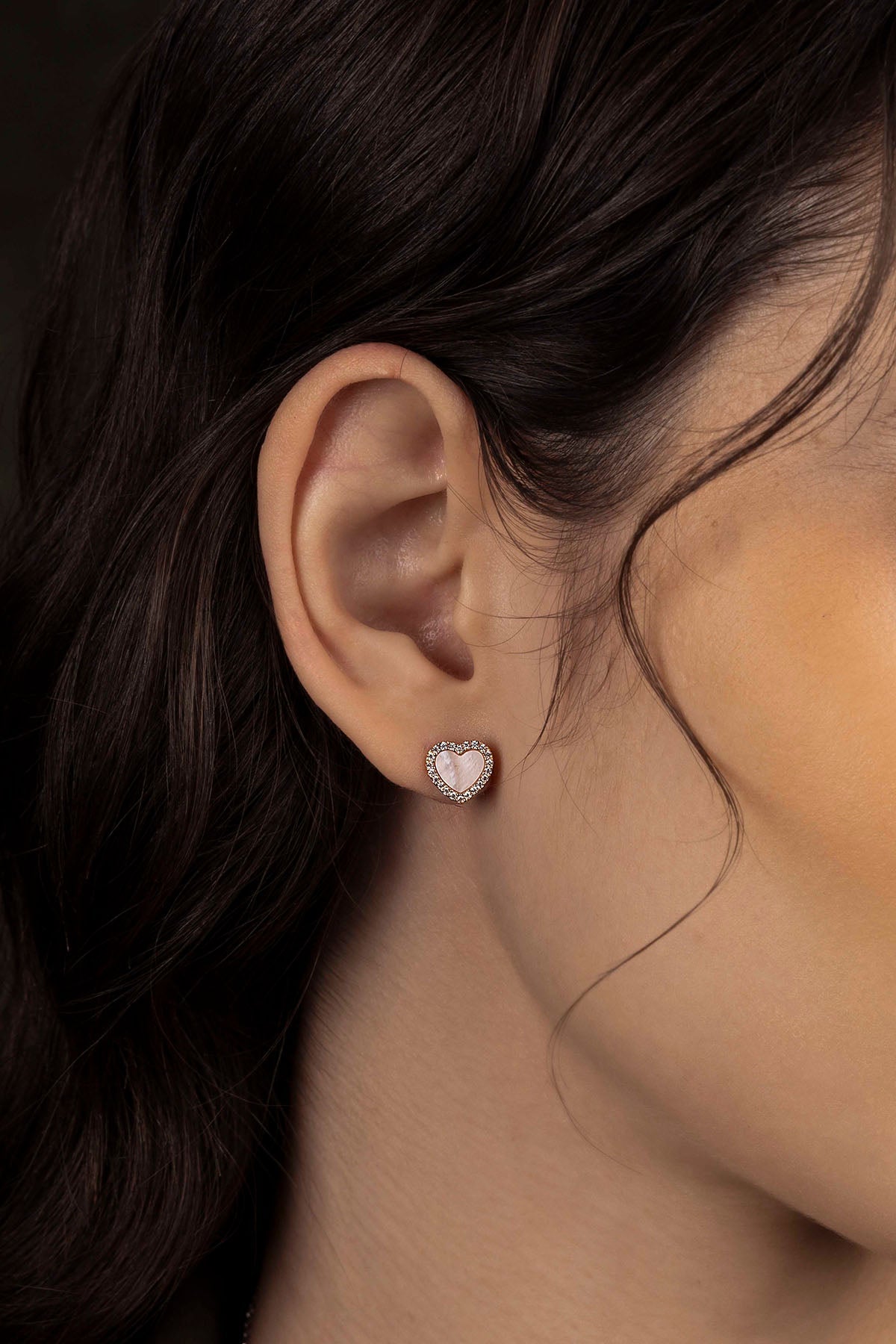Heart-shaped earring worn by a model with dark hair.