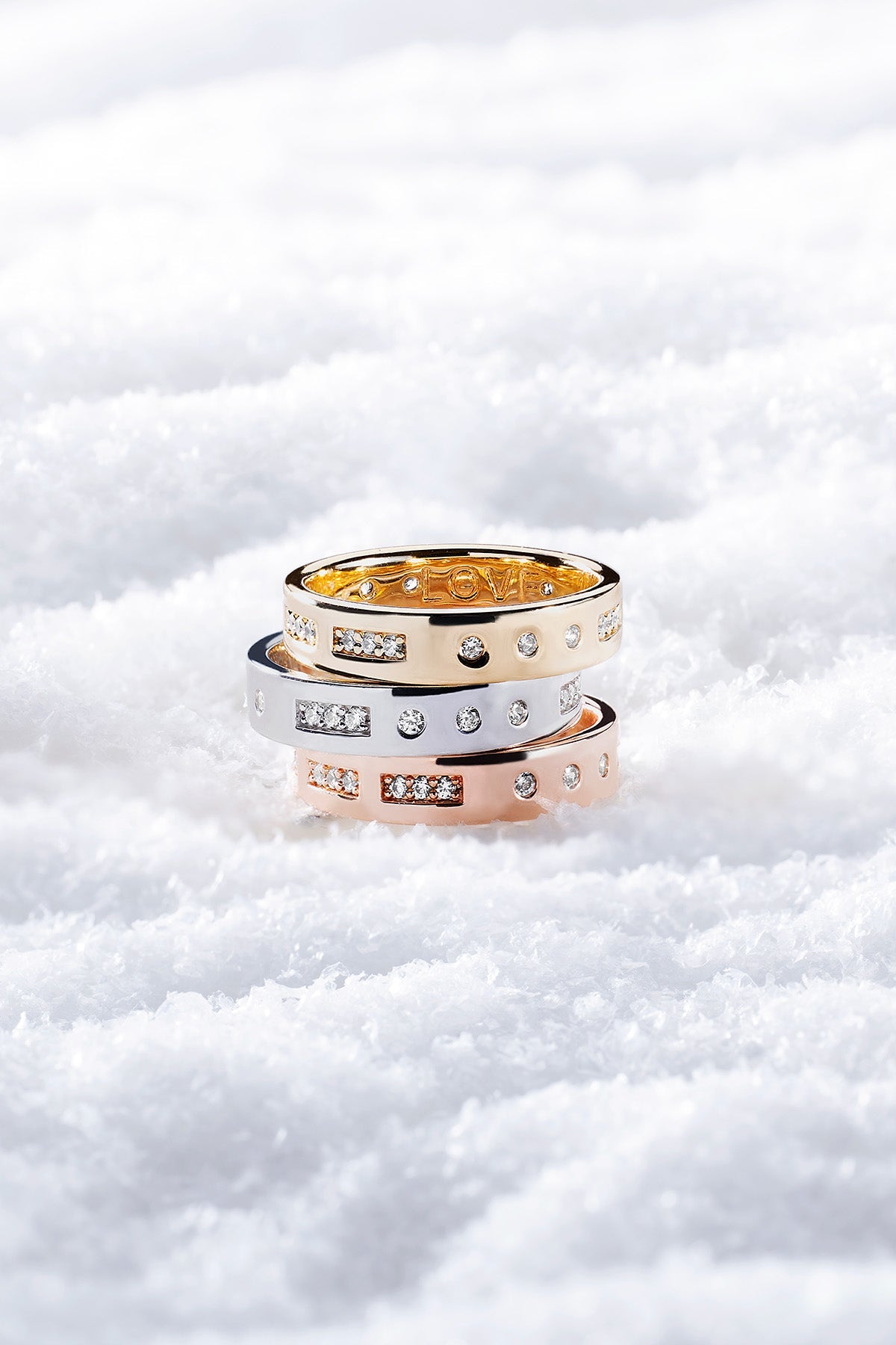 Three gold, silver and rose gold rings stacked on a snowy background