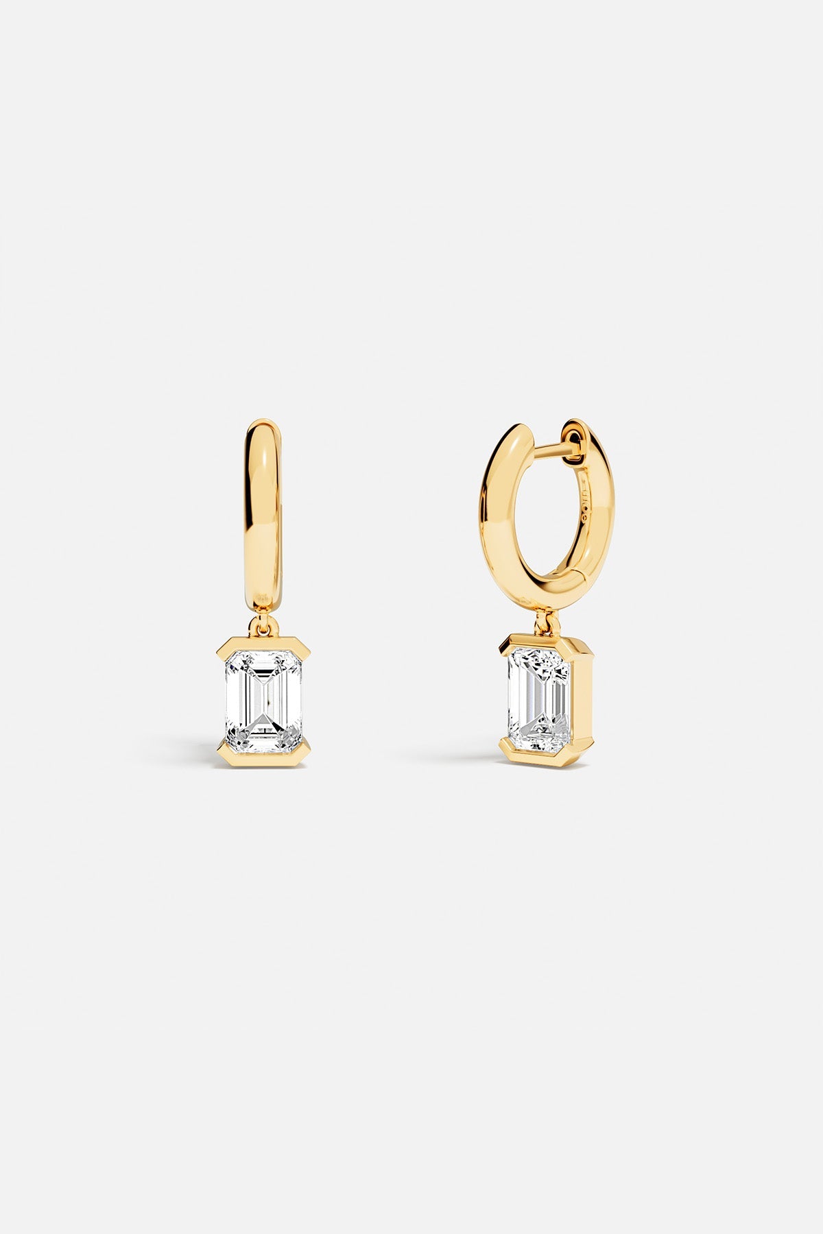 Earrings APM Monaco yellow gold hoop earrings with emerald-cut diamond drops on each hoop.