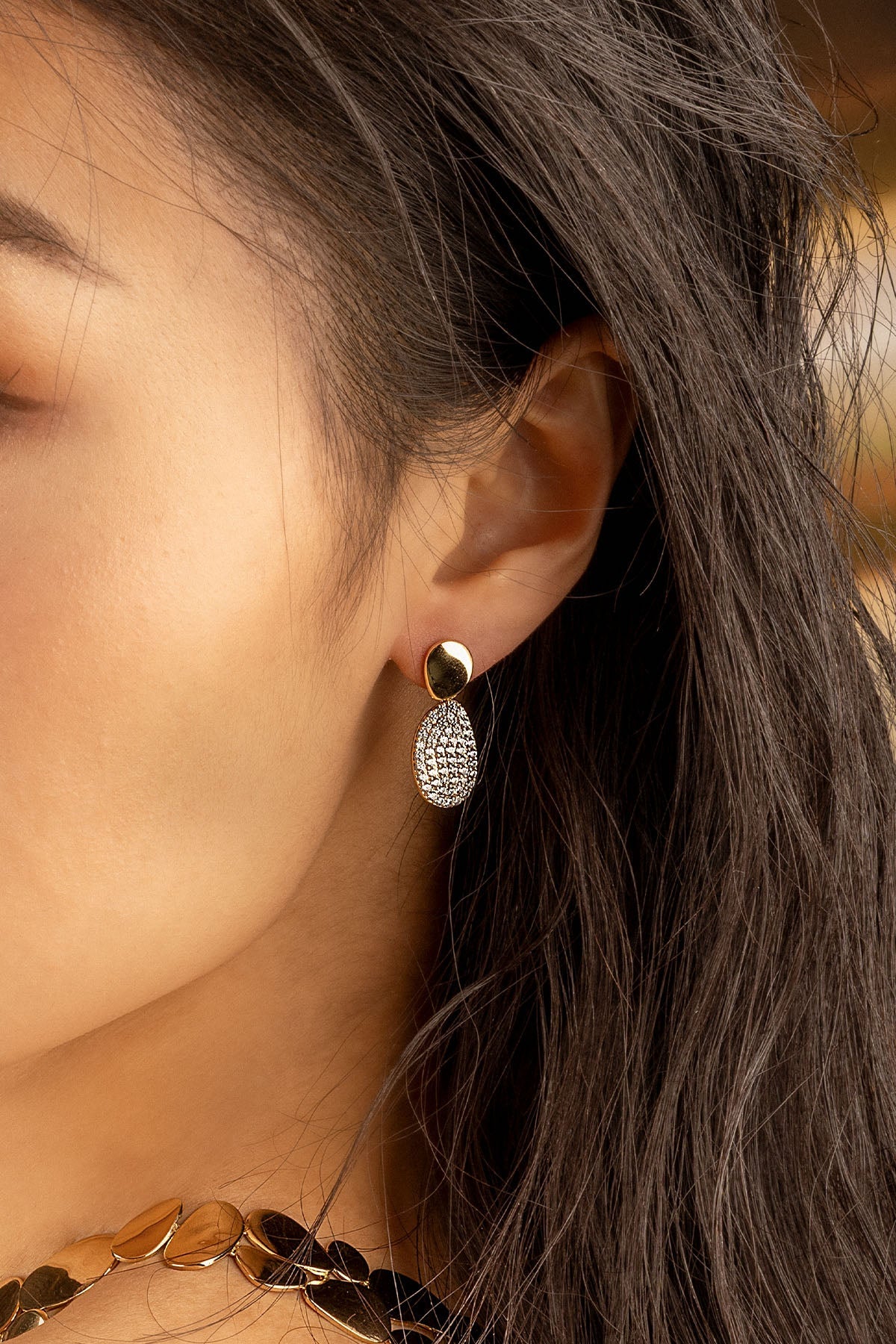 Earrings APM Monaco, yellow gold tone with clear pavé diamante stones in a pebble-shaped design.